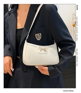 Detail of white baguette bag featuring a golden bow metal buckle and textured leather