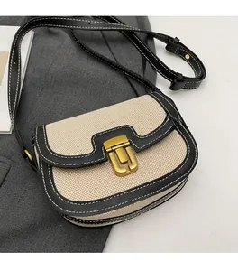Top-down view of canvas and black leather saddle bag with gold metal clasp and white stitching