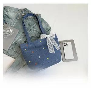 Close-up of blue denim tote bag featuring floral tulip embroidery and white lace bow