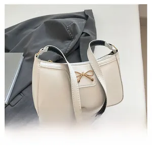Detail of white leather shoulder bag featuring a gold metal bow and bicolor strap