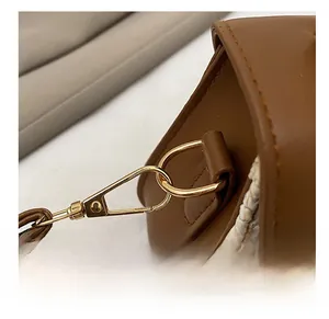 Close-up of golden metal hook and brown leather strap on a woven straw handbag