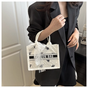 Detail of white tote bag featuring black rose floral embroidery and lace ribbon