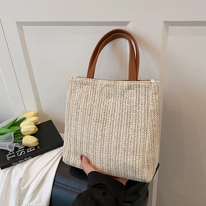 Minimalist straw woven tote bag with brown leather handles on a minimalist display