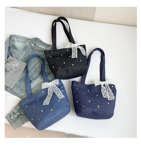 Detailed view of floral embroidery and white lace bows on denim bucket tote bags