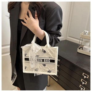 Detail of white tote bag with black rose embroidery, lace bow, and Fashion Bag strap