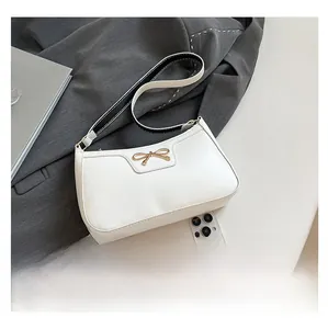 Detail of white leather underarm bag with gold bow clasp and contrast stitch strap