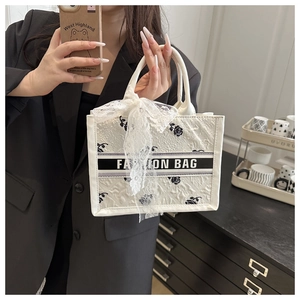 Detail of white tote bag featuring black rose embroidery and a lace bow charm