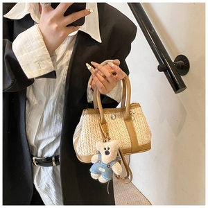 Detail of straw shoulder bag with brown leather trim and a cute bear keychain accessory