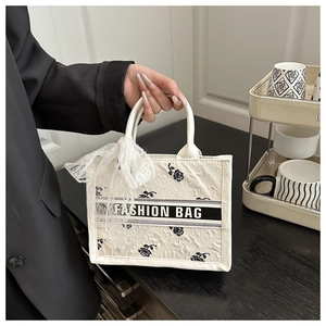 Detailed view of white tote bag featuring black rose pattern and lace bow accessory