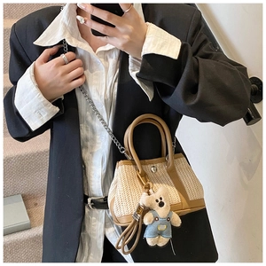 Detail of straw woven crossbody bag featuring a leather handle and cute teddy bear charm