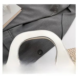 Detail of white leather handbag featuring circular cutout handles and precision stitching