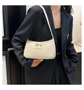 Détail du sac croissant crème avec fermoir nœud doré porté sur un blazer bleu marine