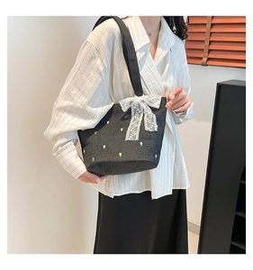 Detail of black denim tote bag with floral embroidery and white lace bow decoration