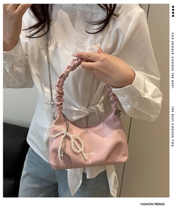 Pink shoulder bag detail showing pleated strap, pearl bow charm, and silver chain detail
