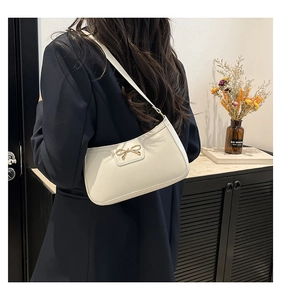 Sac croissant blanc crème avec nœud doré porté par un mannequin dans un décor de style de vie