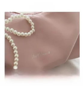 Macro detail of a pale pink leather handbag featuring a white pearl decorative strap