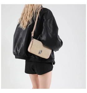 Detail of woven beige shoulder bag with silver logo buckle on black leather jacket