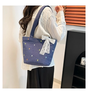 Detail of blue denim tote bag featuring floral embroidery and a white lace bow accent