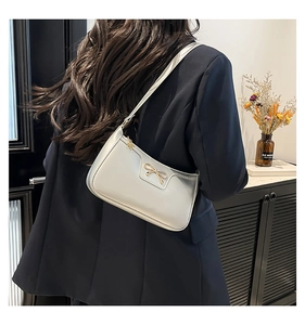 Detail of silver shoulder bag with gold bow ornament worn by model in a modern interior