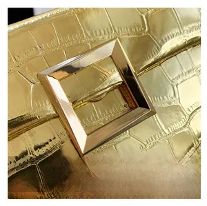 Close-up of golden square metal clasp and crocodile textured leather envelope bag