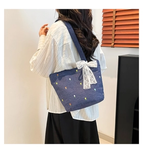 Close-up of floral embroidery and large white lace bow on blue denim tote bag