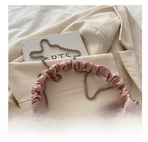 Detail of pink shoulder bag featuring a pleated handle, silver chain, and pearl accents