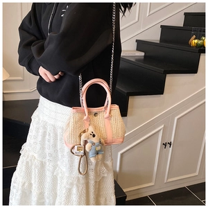 Detail of straw shoulder bag with pink faux leather trim and plush bear charm