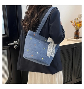 Detail of denim tote bag with floral embroidery and large white lace bow accessory