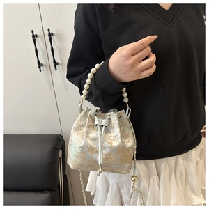 Detail of blue brocade bucket bag with pearl handle and gold tree embroidery on model
