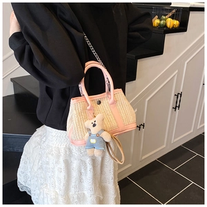 Pink patchwork straw tote bag with bear charm shown worn on a shoulder over casual outfit