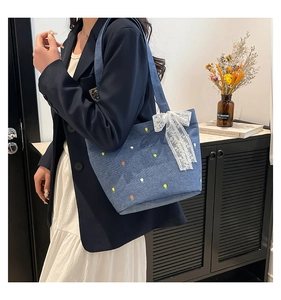 Close-up of floral embroidery and white lace bow detail on a blue denim tote bag