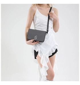 Detail of grey textured crossbody bag with silver interlocking metal logo and leather strap