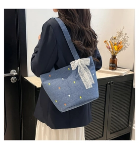 Detail of embroidered floral patterns and white lace bow on the blue denim tote bag