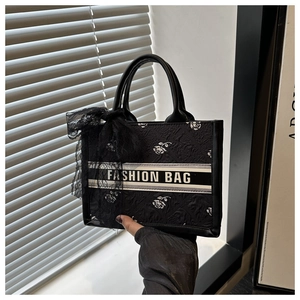 Detail of black tote bag with white rose pattern and a chic black lace bow charm