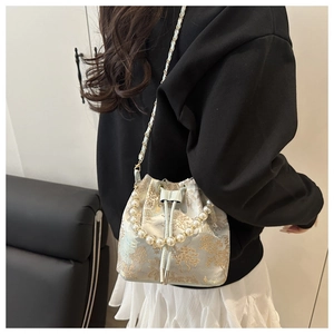 Detail of embroidered bucket bag with pearl handle and golden landscape pattern