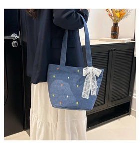 Detail of denim tote bag with colorful flower embroidery and white lace ribbon bow