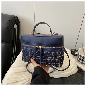 Close-up of navy blue tweed box bag featuring gold zipper and textured woven details