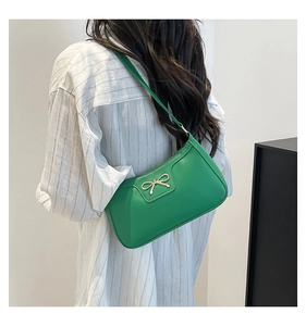 Détail d'un sac sous le bras en cuir vert vif avec un nœud doré porté par un mannequin