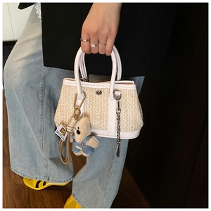 Detail of straw handbag with white leather trim, silver chain, and cute bear pendant
