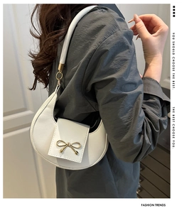 Side view of a white minimalist crescent underarm bag with a gold bow on a model