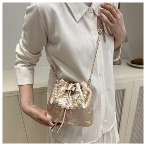 Close-up of golden floral embroidery on pink satin silk pearl bucket bag with metal chain