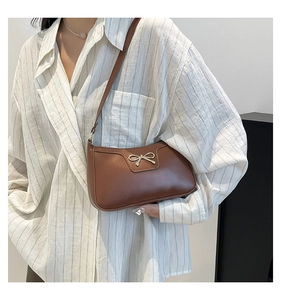 Close-up of brown leather crescent bag with a decorative silver bow and sleek strap