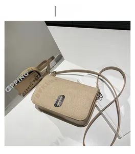 Detail of khaki straw textured crossbody bag with silver metal logo and leather strap