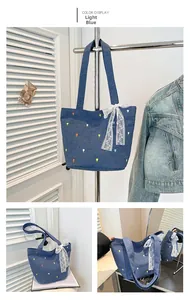 Detail of light blue denim tote bag featuring floral embroidery and a white lace bow