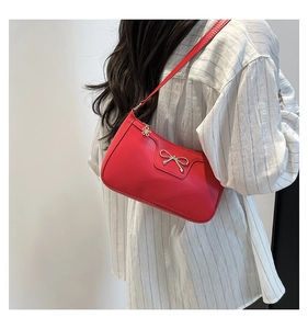 Détail du sac croissant rouge avec nœud argenté et breloque fleurie sur la fermeture