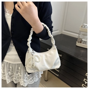 Detail of white pleated crescent bag featuring pearl bow charm and cloud-style handle