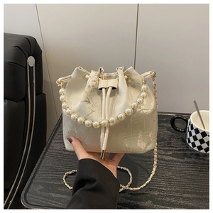Detailed close-up of Chinese embroidery and pearl handle on a cream bucket bag