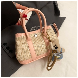 Detail of straw shoulder bag with pink faux leather trim and a cute teddy bear pendant