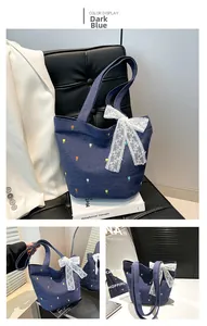 Detail of blue denim tote bag featuring floral embroidery and a large white lace bow