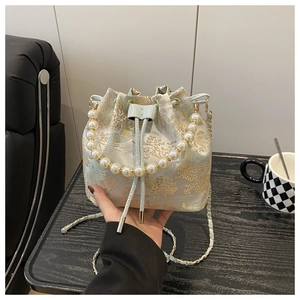 Detail of embroidered satin bucket bag featuring pearl handle and gold chain strap